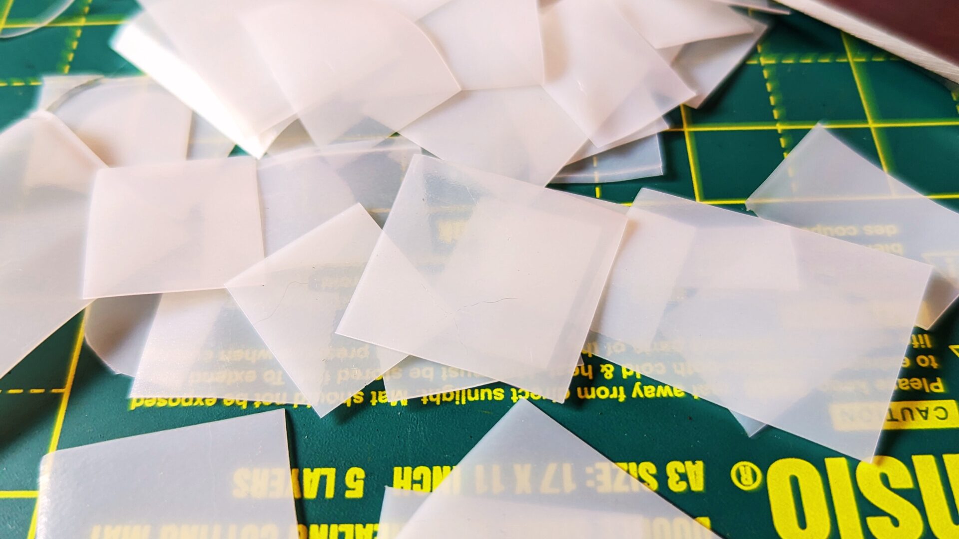 Plastic from an opaque white milk bottle cut into squares, on a work surface.