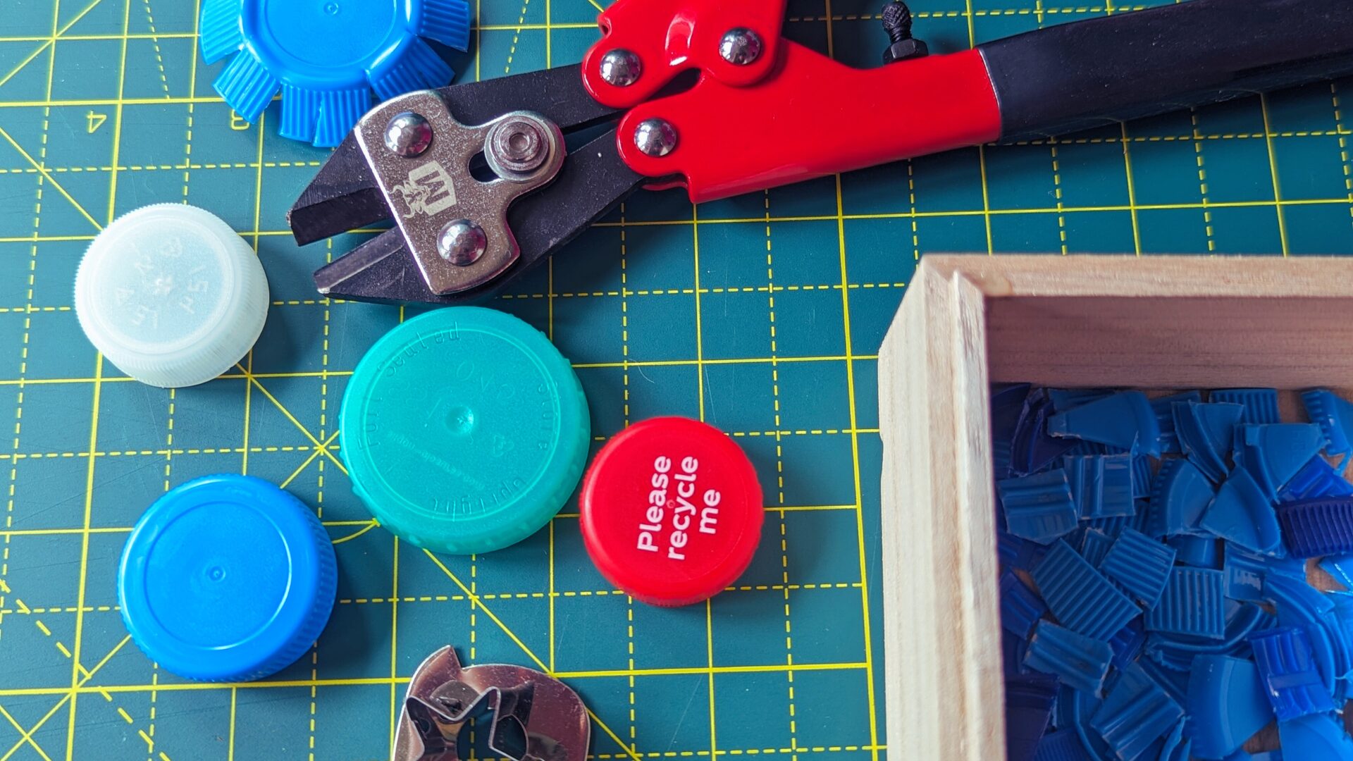 Some plastic bottle caps with bolt cutters and a cookie cutter on a work surface