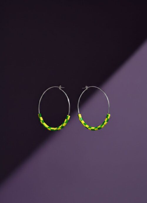 A pair of silver tone hoop earrings with yellow and green beads made from upcycled materials, on a purple background