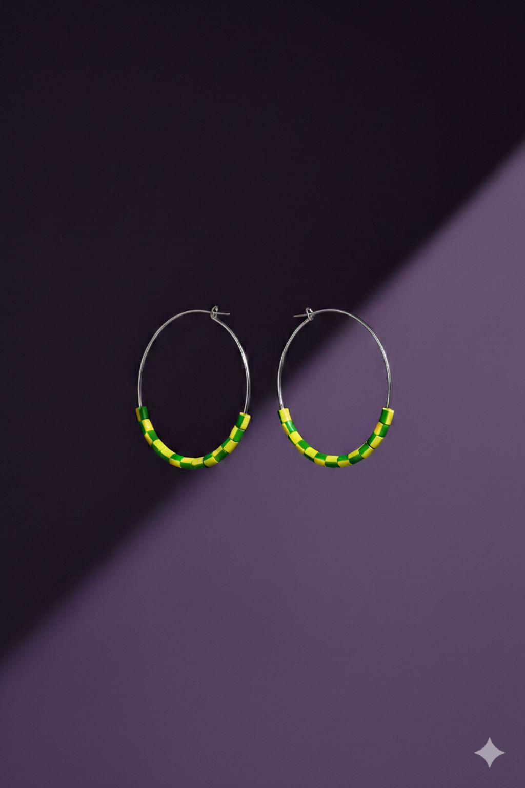 A pair of silver tone hoop earrings with yellow and green beads made from upcycled materials, on a purple background