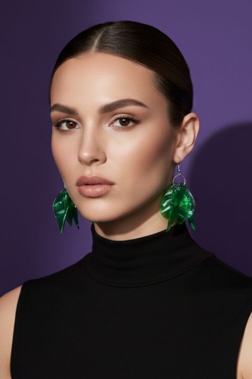 A woman wearing a pair of silver tone earrings with green charms, upcycled from waste plastic