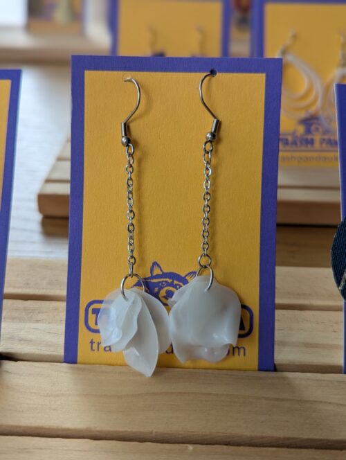 Dangly earrings with white petals pictured on a jewellery display card
