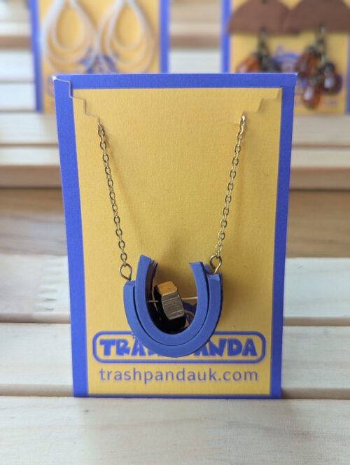 A gold chained necklace with a unique purple rubber and gold bolt pendant, on a jewellery display card