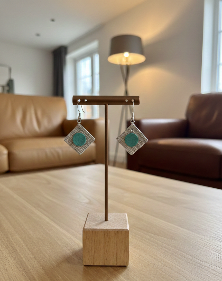 A display rod with Textured Squared earrings made from recycled leather A display rod is on a coffee table with a pair of square leather earrings hanging from it. In the background there are leather sofas and a lamp