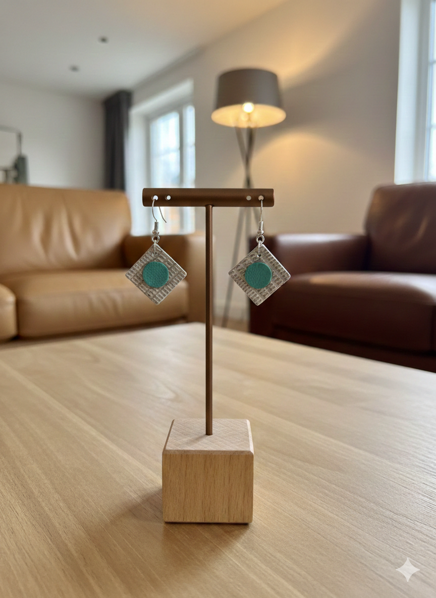 A display rod is on a coffee table with a pair of square leather earrings hanging from it. In the background there are leather sofas and a lamp