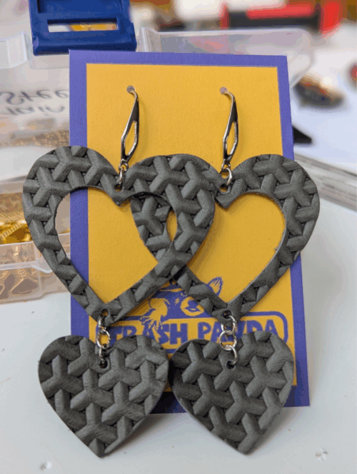 A pair of earrings - heart shaped and made from grey basket weave leather - on a jewellery display card