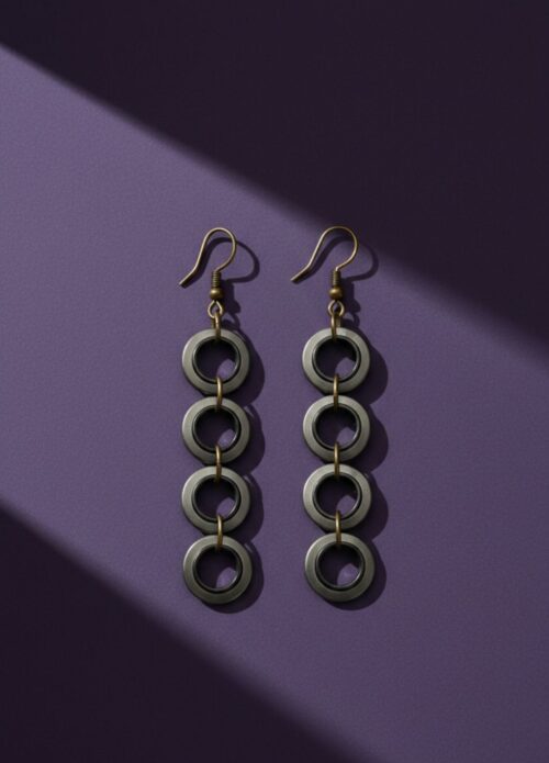A pair of industrial-style earrings made from upcycled materials, they are dangly with 4 small rings hanging. On a purple background