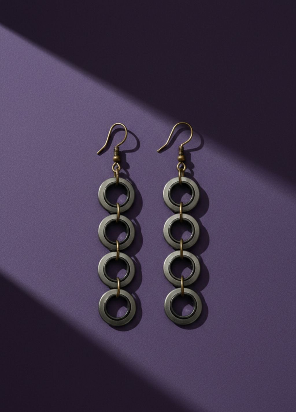 A pair of industrial-style earrings made from upcycled materials, they are dangly with 4 small rings hanging. On a purple background