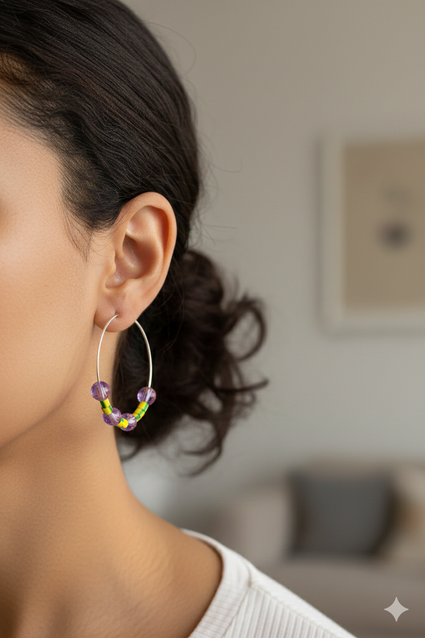 A woman wearing large hoop earrings with lilac and yellow beads. They are made from upcycled electrical wire covers.