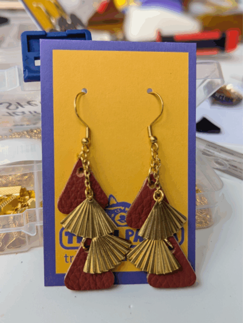 A pair of dangly earrings made with red leather and brass-multi-drop, on a brightly coloured earring display card