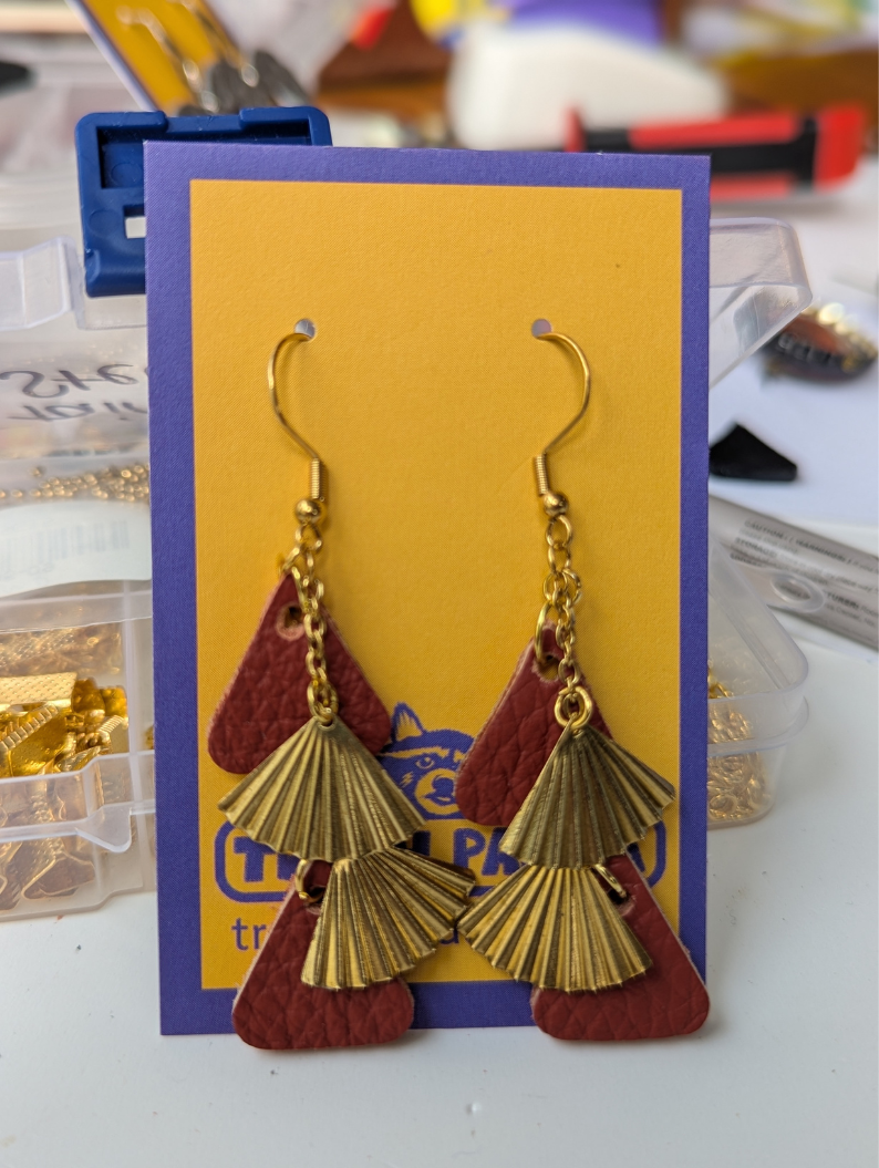 A pair of dangly earrings made with red leather and brass-multi-drop, on a brightly coloured earring display card