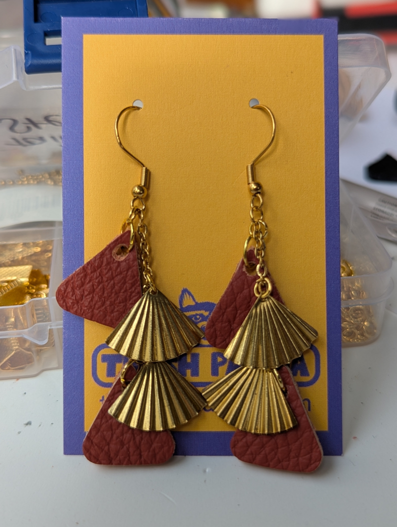 A pair of dangly earrings made with red leather and brass-multi-drop, on a brightly coloured earring display card