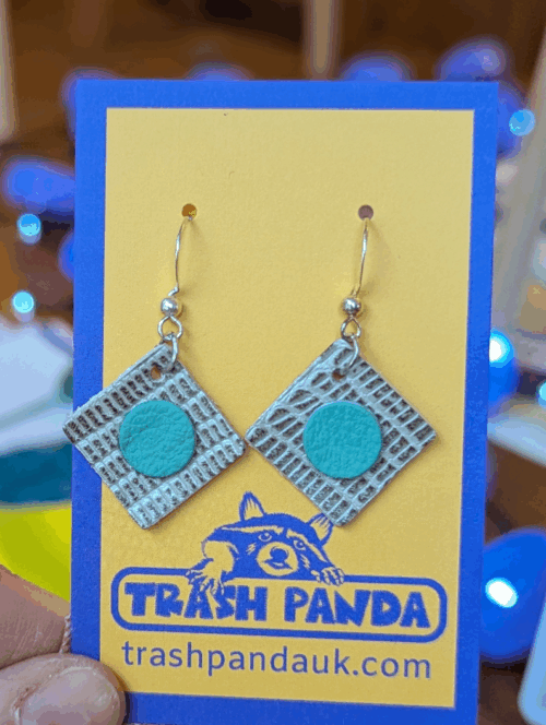 Dangly earrings made from upcycled leather offcuts. On a jewellery display card and held by a hand