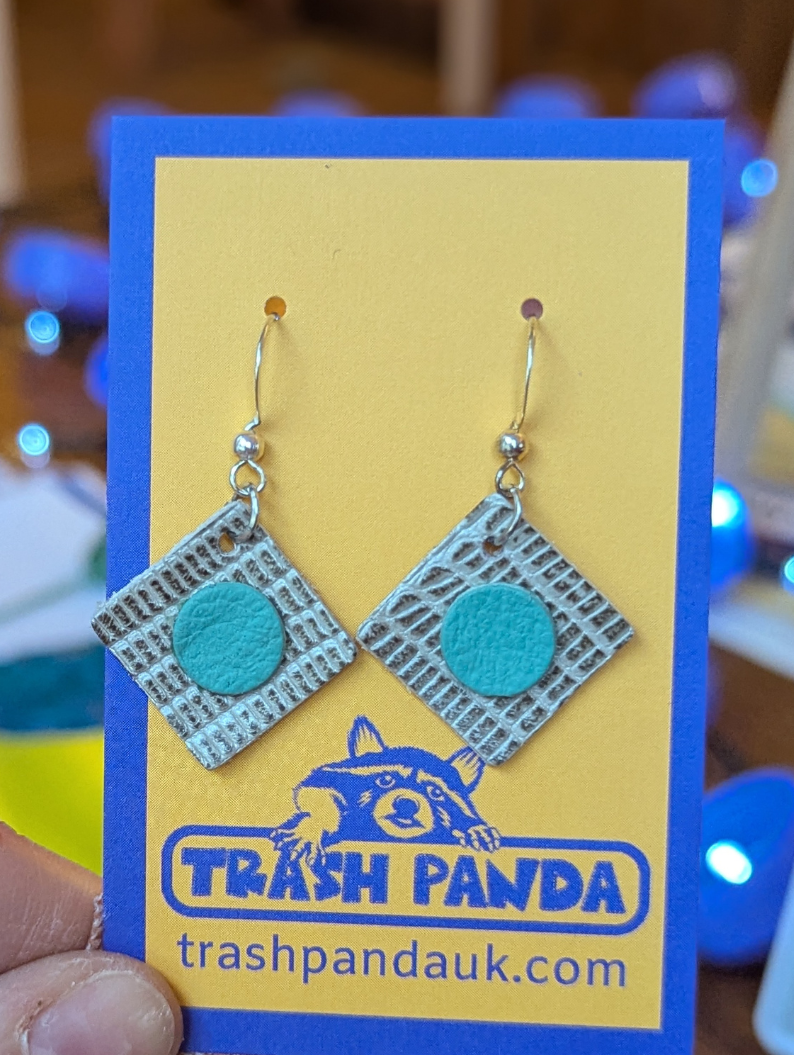 Dangly earrings made from upcycled leather offcuts. On a jewellery display card and held by a hand