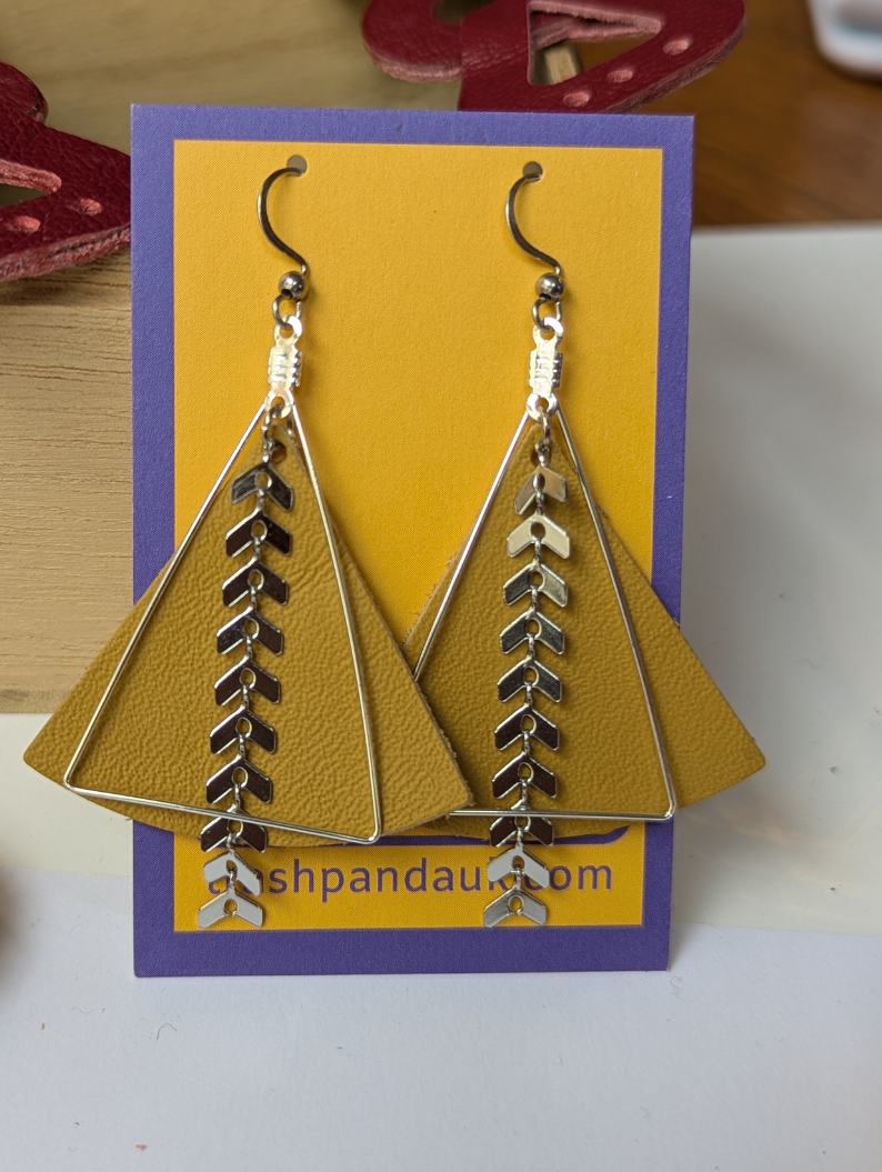 A pair of earrings - mustard leather with silver-tone detail on them - are on a jewellery card