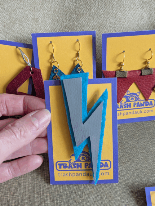 Upcycled lightning bolt brooch made from electric blue felt and a silver inflatable offcut, displayed on a Trash Panda backing card, held by a hand