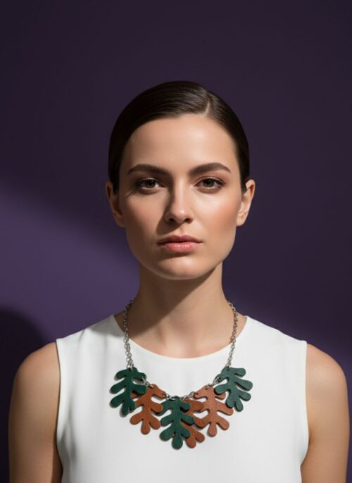 A woman wearing A necklace made from a silver tone chain and oak-shaped leaves cut from leather, on a purple backgound