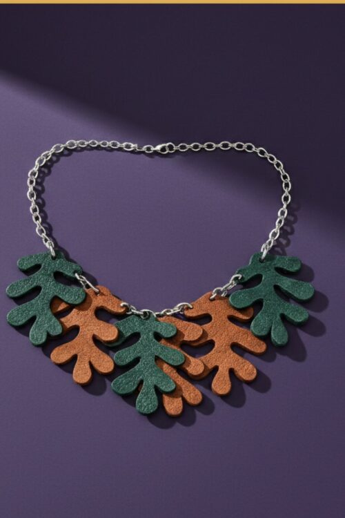 A necklace made from a silver tone chain and oak-shaped leaves cut from leather, on a purple backgound