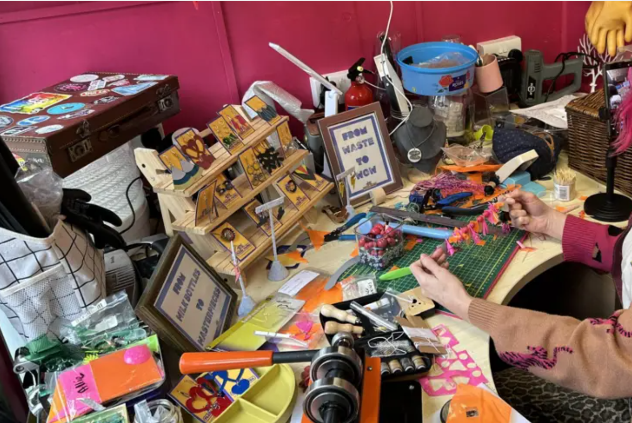 A woman sat at a desk at a studio making jewellery. She is holding a necklace that's made from waste inflatables