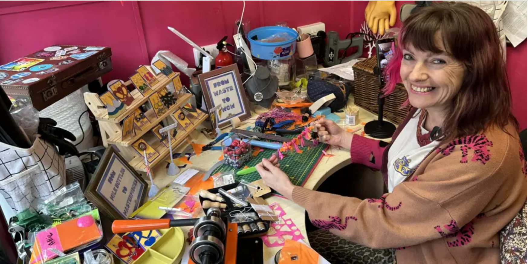 Louise Lea Trash Panda on BBC Radio Solent with her inflatable jewellery A woman sat at a desk at a studio making jewellery. She is holding a necklace that's made from waste inflatables