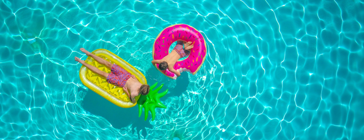 A wide shot of a blue pool with two floating pool toys - one rubber ring and another pineapple shaped lilo