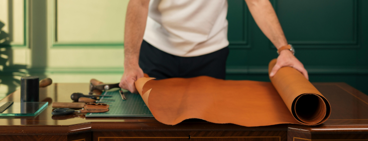 A man rolling out a large piece of tan-coloured leather on a workbench